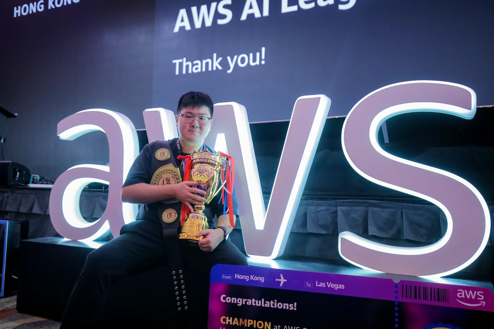 Max Chui with the AWS AI League championship trophy and belt on stage at AWS Summit Hong Kong